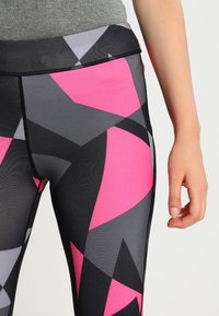 Leggings coloridos con un patrón geométrico en rosa, gris y negro. Fabricados con un tejido elástico, tienen una textura suave y una cinturilla elástica.