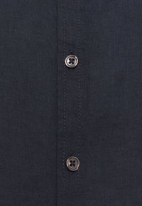 Tissu de chemise en lin navy avec une texture lisse, comportant une rangée de boutons de couleur métallique sombre et des détails de couture contrastants.
