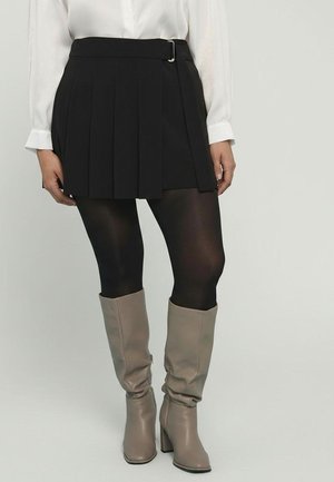 Czarna plisowana mini spódniczka z paskiem i srebrną klamrą, zestawiona z czarnymi rajstopami i beżowymi kozakiem za kolano o lekkim połysku.