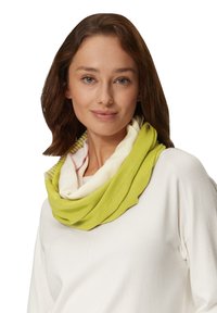 Groene en crèmekleurige infinity sjaal met gelaagde texturen en een subtiel visgraatpatroon. Zacht materiaal valt rond de nek.