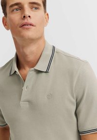 Polo shirt grigio chiaro con tessuto testurizzato, dotato di un collo a strisce blu navy e un'apertura con due bottoni, e piccolo logo ricamato sul petto.