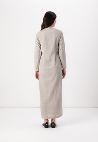 Dlhé, šedé šaty s vzorom a dlhými rukávmi, so subtilným bodkovaným dizajnom. Hladká látka sa kĺže až po členky, skombinované s čiernymi topánkami.