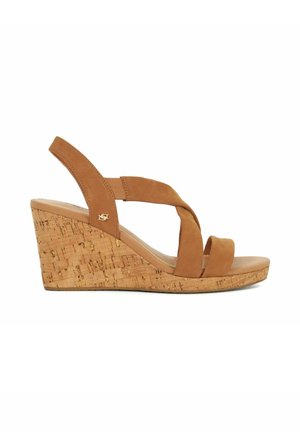 Sandales compensées en suède beige avec une base en liège, dotées de sangles croisées et d'une semelle lisse. Texture en liège visible sur la semelle compensée pour une meilleure adhérence.