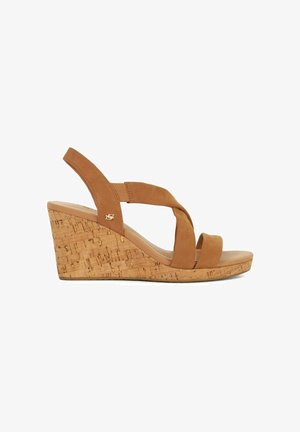 Sandales compensées en suède beige avec une base en liège, dotées de sangles croisées et d'une semelle lisse. Texture en liège visible sur la semelle compensée pour une meilleure adhérence.
