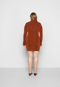 Vestido em tom ferrugem com acabamento texturizado, mangas longas e detalhes em botão nos punhos. Silhueta ajustada que termina à altura da coxa.