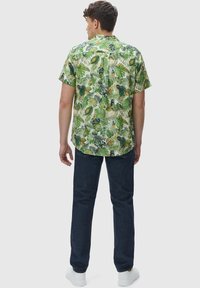 Camicia a maniche corte realizzata in tessuto leggero, con stampa di foglie tropicali verdi e uccelli. Abbinata a jeans blu scuro e sneakers bianche.