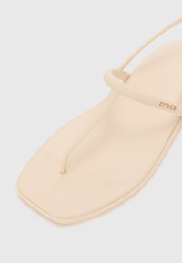 Beige kumppariflip-flop minimalistisella muotoilulla. Varustettu thong-hihnalla, litteällä pohjalla ja tekstuurilla varustetulla sisäpohjalla, jossa on huomaamaton logo.