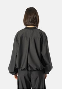 Czarna kurtka bombowca o luźnym kroju, z rękawami raglanowymi i elastycznym wykończeniem. Gładki materiał o matowym wykończeniu, zaprojektowana dla swobodnej sylwetki.