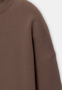 Sweat-shirt marron à manches longues avec col côtelé et détails de coutures visibles sur le haut du bras et la zone de l'épaule.