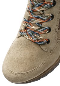 Beiger Wildlederschuh mit mehrfarbigen, geflochtenen Schnürsenkeln, die durch schwarze Metallösen gezogen sind, zeigt die Zehe und einen Teil der Sohle.