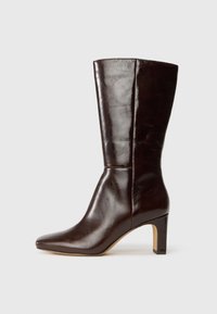 Bota de cuero marrón oscuro a media pantorrilla con punta afilada y tacón cuadrado, mostrada en perfil derecho sobre un fondo claro y liso.