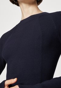 Granatowy sweter dziany z teksturowanymi, prążkowanymi akcentami, dopasowanym krojem i okrągłym dekoltem. Posiada długie rękawy i gładką tkaninę.