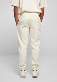 Cremefarvede sweatpants lavet af blødt stof, med en enkelt baglomme og tapered ben, parret med hvide træningssko.