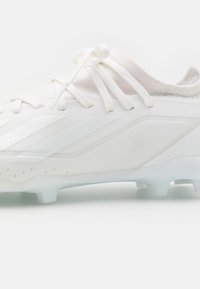 Scarpino da calcio bianco con una parte superiore in sintetico liscio, dettagli testurizzati e una suola traslucida con molteplici tacchetti per una migliore trazione.