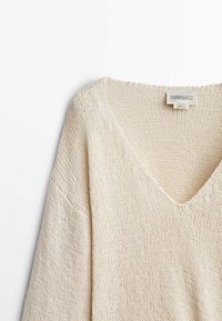 Pull en tricot couleur crème avec un décolleté en V profond, des manches larges et une finition texturée. L'étiquette indique "Massimo Dutti Édition Limitée."