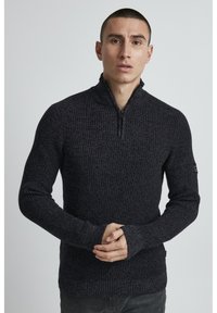 Dunkelgrauer Pullover mit einem strukturierten Strickdesign, hohem Kragen und halblangem Reißverschluss. Mit gerippten Bündchen und einem kleinen Logo am Ärmel.