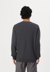 Sudadera gris oscuro con cuello redondo, mangas largas y puños de canalé. Tejido suave con detalles de costura mínimos, vista trasera lisa.