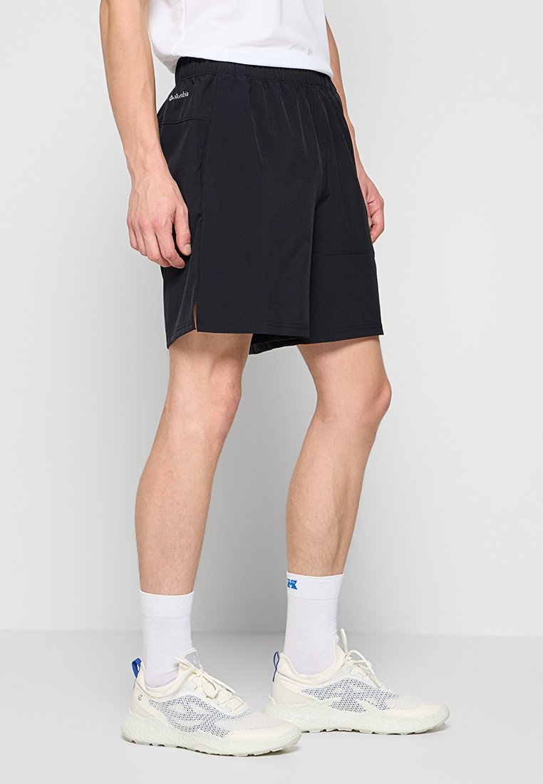 Pantalones cortos deportivos negros con cinturilla elástica, bolsillos laterales y pequeñas aberturas en el dobladillo. Combinados con calcetines blancos y zapatos claros.