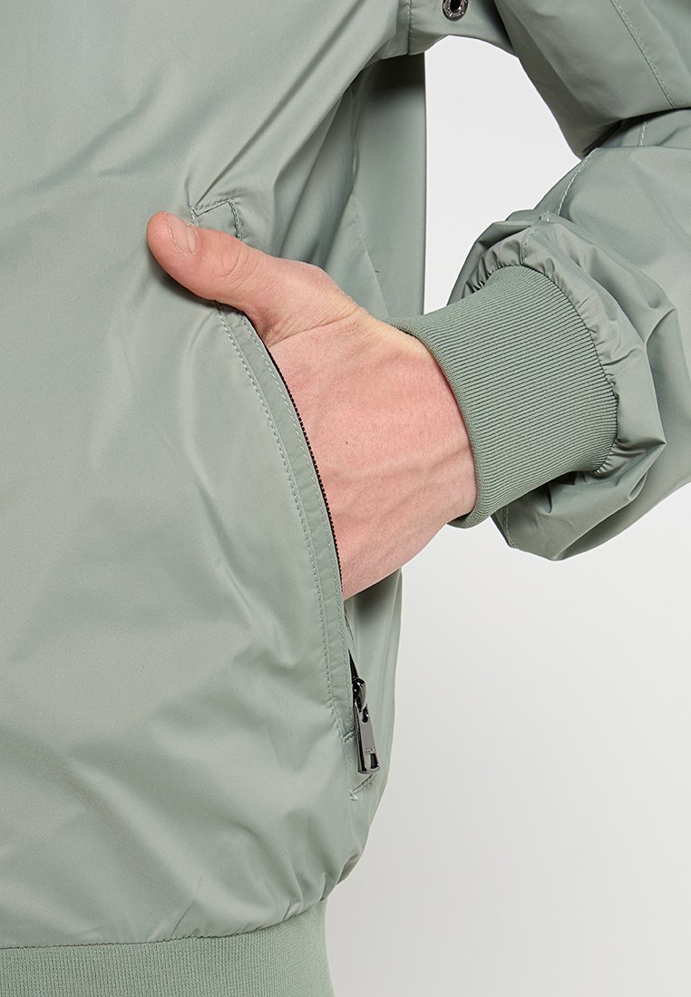 Grüne Nylon-Bomberjacke mit einem Reißverschluss-Seitentasche, elastischen Bündchen und einer glatten Textur. Minimalistisches Design mit lässiger Passform.