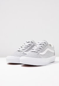 Baskets scintillantes argentées avec accents blancs, dotées d'un design bas, d'un bout rond et d'une fermeture à lacets. Surface texturée et semelle en caoutchouc plate.