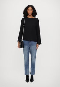 Μαύρη υφασμάτινη μπλούζα με μακριά μανίκια, συνδυασμένη με ανοιχτό κυανό παντελόνι σε ίσια γραμμή. Το μοντέλο κρατάει μια μικρή μαύρη τσάντα και φοράει μυτερές μαύρες μπότες μέχρι τον αστράγαλο.