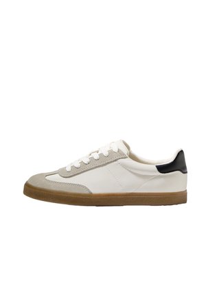 Weiße Sneaker mit grauen Wildlederakzenten, schwarzer Ferse, flacher Schnürung und einer strukturierten braunen Gummisohle. Klassisches Design mit niedriger Form.