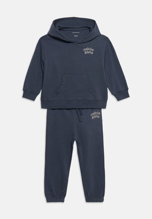Ensemble pour enfants bleu foncé avec sweat à capuche et pantalon jogger, logo Calvin Klein sur la poitrine et la cuisse, poignets élastiques et poche kangourou à l'avant du sweat.