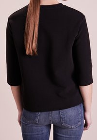 Svart, ribbat jersey-top med trekvartslånga ärmar, rundad halsringning och en avslappnad passform, tillsammans med jeans i denim som visar bakfickor.