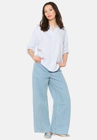 Mėlynos ir baltos dryžuotos marškiniai su ilgomis rankovėmis, derinami su plačiais mėlynais džinsais. Komplektą papildo sukritę rankovės ir priekiniai kišeniai.