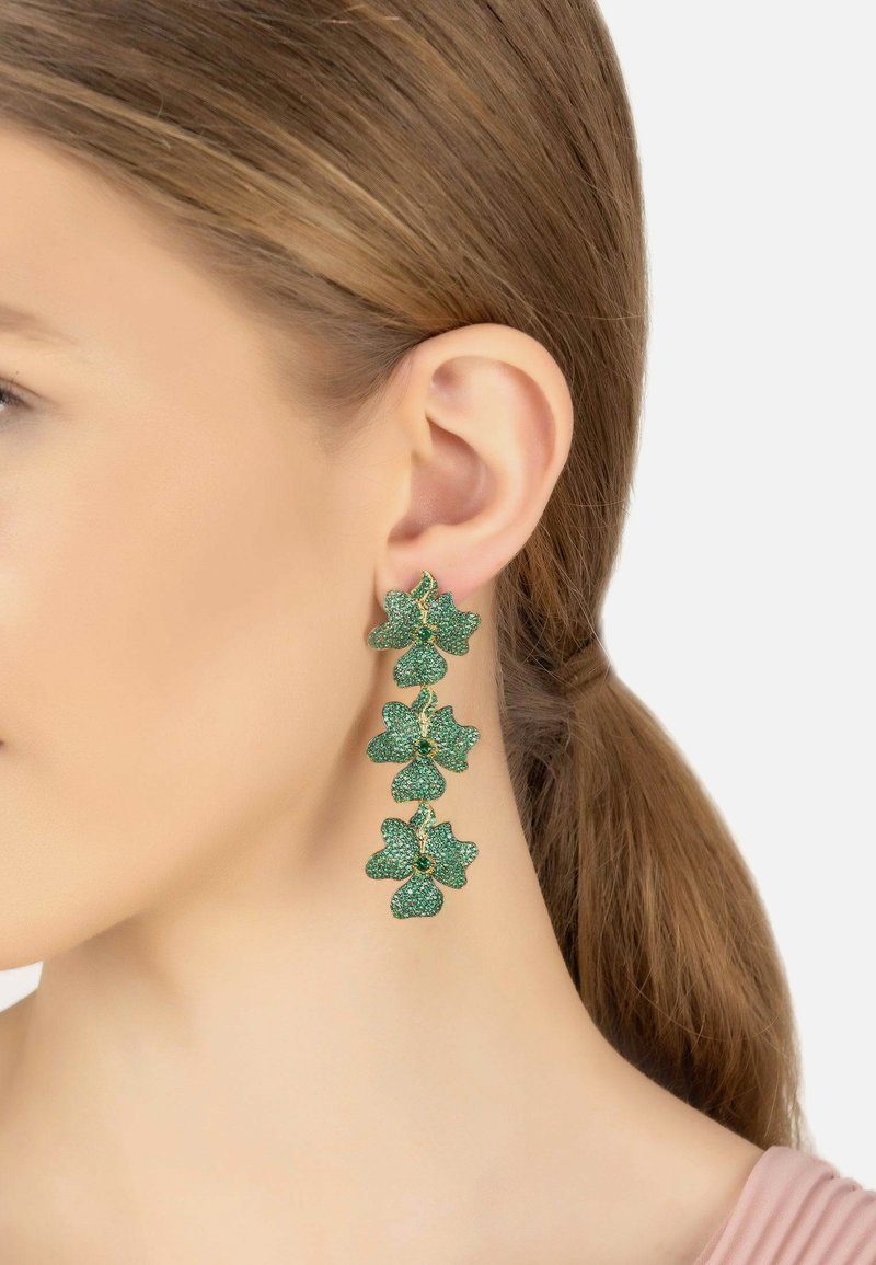 Green floral earrings made of metal with a textured, sparkling finish. Features layered leaf designs accented with small blue gemstones.