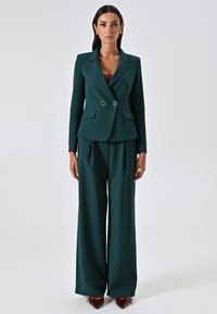 Abito teal composto da un blazer aderente con doppio bottone, due tasche frontali e pantaloni a gamba larga. Tessuto liscio e strutturato con un design elegante.