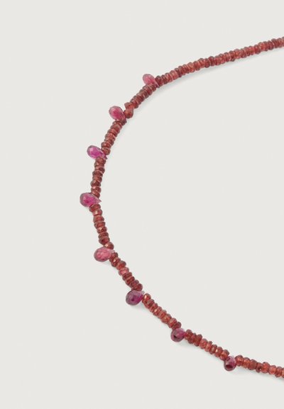 Karoliai, kuriuose yra lygūs, apvalūs raudoni ir rožiniai brangakmeniai su facetuotu paviršiumi, kaitaliuojasi per vėrinio dizainą.