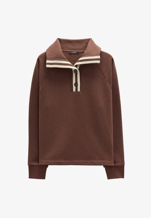 Brązowy sweter z miękkiego materiału o luźnym kroju. Posiada paskowany kołnierz w kolorze kremowym i brązowym oraz dwa brązowe guziki przy szyi.