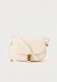Krémová kožená kabelka přes rameno s klopou, zlatým kováním a páskem se zavázáním na uzel. Hladká textura a zaoblený tvar.