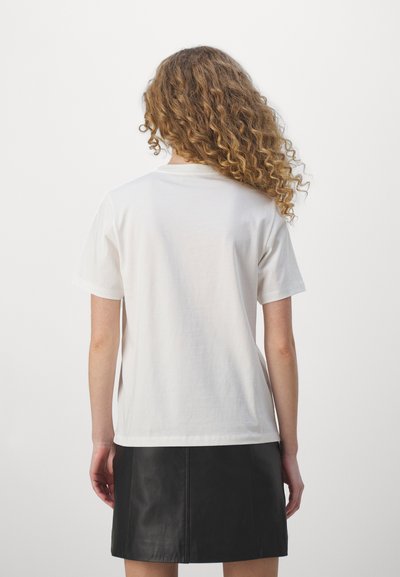 T-shirt en coton blanc avec un col ras du cou et des manches courtes, vu de dos, associé à une jupe en cuir noir. Texture lisse, design simple.