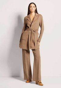 Bruine, gebelte blazer met revers en twee voorzakken, gecombineerd met bijpassende wijde broek. Heeft een gladde textuur en strakke lijnen.