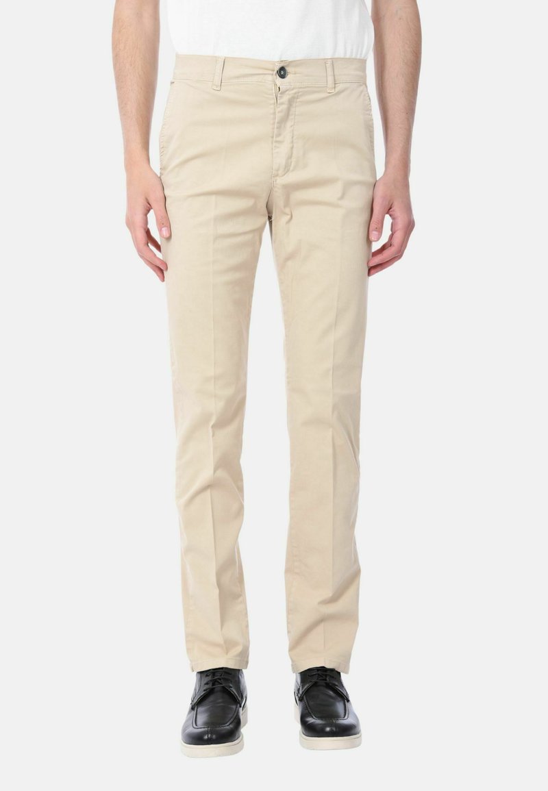 Chinos beige con taglio dritto, realizzati in cotone, dotati di chiusura con bottone e tasche laterali. Indossati con scarpe nere.
