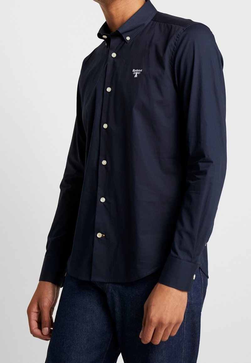 Laivastonsininen pitkähihaisen paita nappikauluksella, jossa pienen valkoisen logon rinnassa ja vaaleat napit edessä napituksessa.