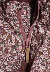 Blomstermønstret jakke i lilla, med en sentralslushing og en rosa draknop. Materialet ser ut til å være teksturert og mykt.