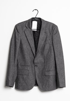 Grauer Fischgrät-Blazer mit Kerbkragen, zwei vorderen Klappentaschen, Ein-Knopf-Verschluss, hängend an einem schwarzen Bügel mit weißem Etikett.