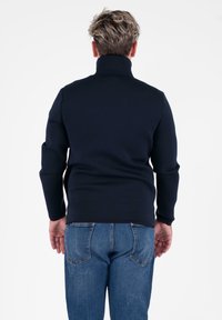 Maglione a collo alto blu navy realizzato in tessuto lavorato a maglia, con maniche lunghe e design aderente. Indossato con jeans in denim azzurri.