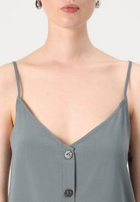 Top gris sin mangas con diseño de escote en V, que presenta tirantes finos y tres botones circulares en la parte delantera, hecho de una tela suave.