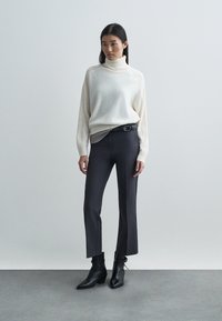 Κρέμα πλεκτό πουλόβερ με ριμπ ύφανση, συνδυασμένο με σκούρες εφαρμοστές παντελόνες και μαύρες μπότες μέχρι τον αστράγαλο. Απλός, μοντέρνος σχεδιασμός.