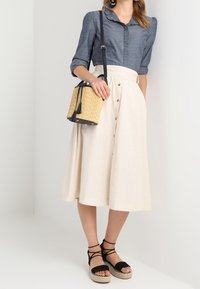Chemise en lin bleu avec détails en boutons, jupe A-line crème avec boutons à l'avant, sandales espadrilles noires et un petit sac tiss é avec des franges.
