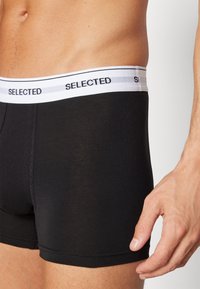 Boxeri negri din bumbac cu o talie albă pe care este inscriptionat "SELECTED." Prezintă o potrivire confortabilă și o textură netedă, evidențiind un design minimalistic.