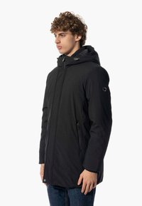Giacca nera con cappuccio, chiusura con zip e tasche laterali. Realizzata in tessuto liscio, presenta una vestibilità morbida e un design minimalista.