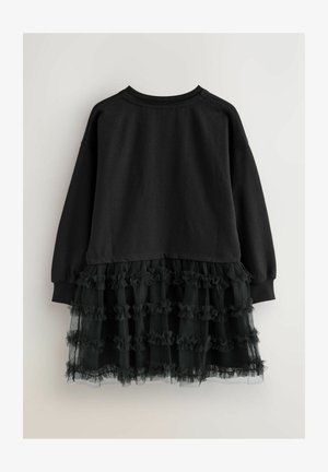 Crna haljina s duksericom dugih rukava i suknjom od tila s volanima. Gornji dio je potpuno crn, dok suknja ima slojevite volane.