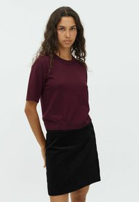 Pull à manches courtes bordeaux avec un col rond, associé à une jupe en velours côtelé noire dotée de deux boutons sur le côté.