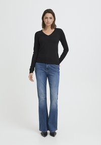 Mustast venivast materjalist pikkade varrukatega ja V-kaelusega kampsun, paaritatud siniste lehvikpõlvedega teksade ja mustade teravate ninaga kontsakingadega. Minimalistlik disain.