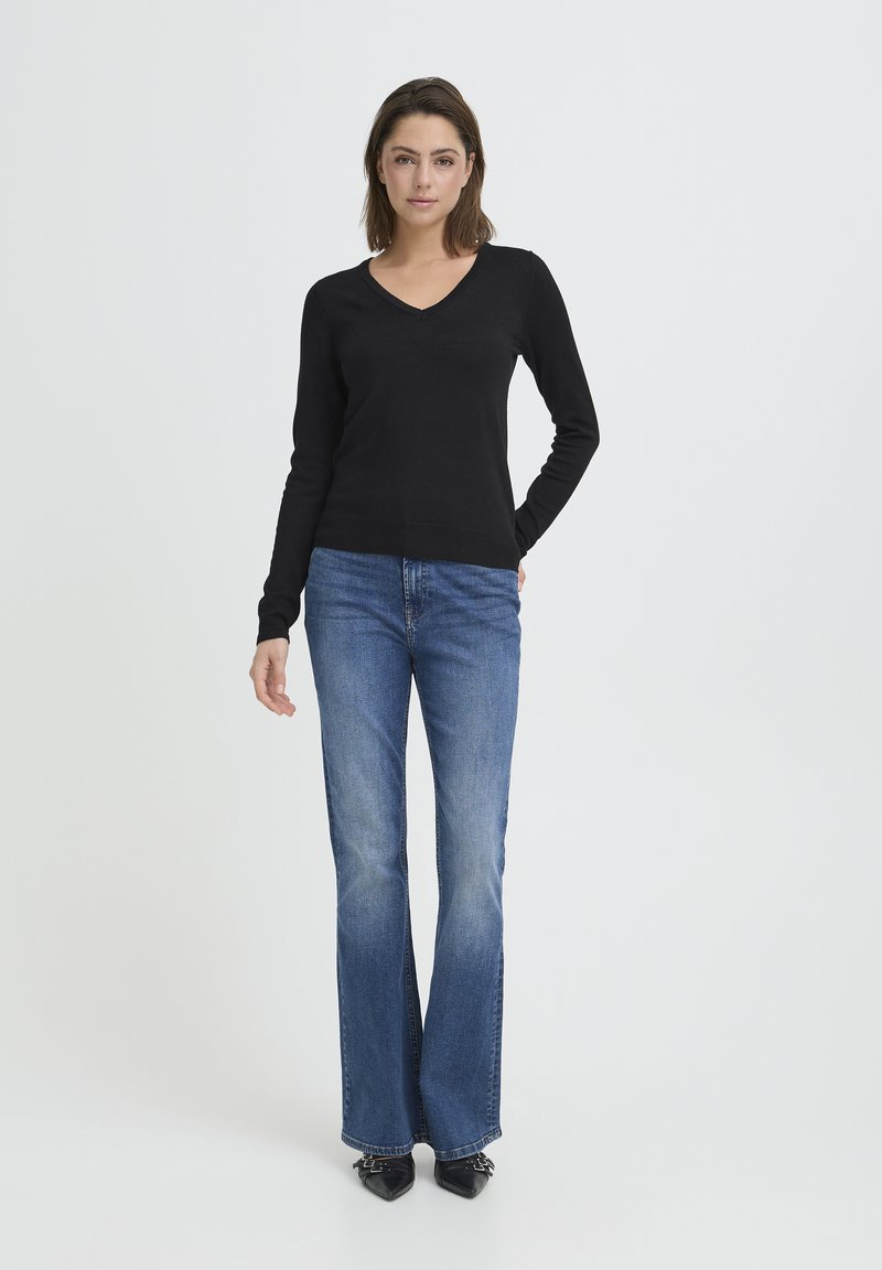 Pull noir cintré à manches longues et col en V, associé à un jean évasé bleu et des escarpins noirs à bouts pointus. Design minimaliste.